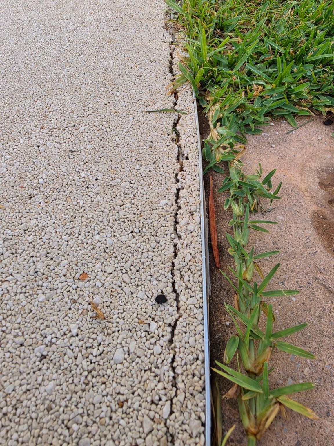 Cracking along the edge of a damaged resin bound surface beside grass